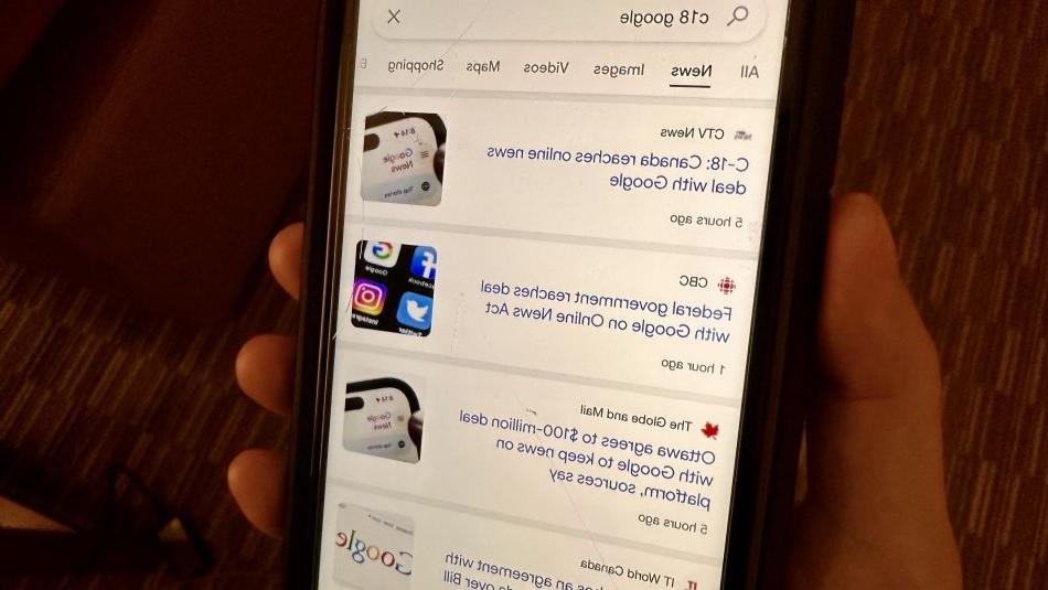A cell phone being held by a hand, showing Canadian news from Google.