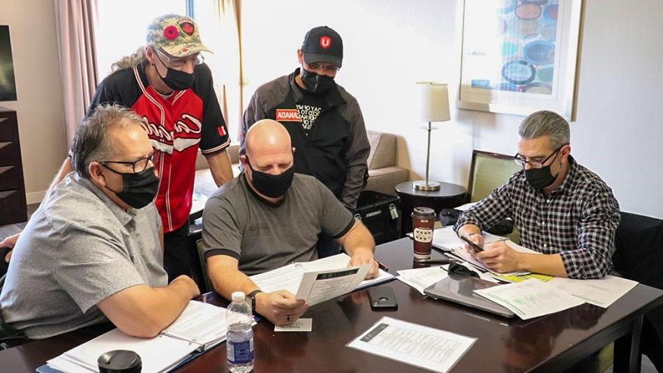 五名戴着口罩的工会成员正在检查谈判文件