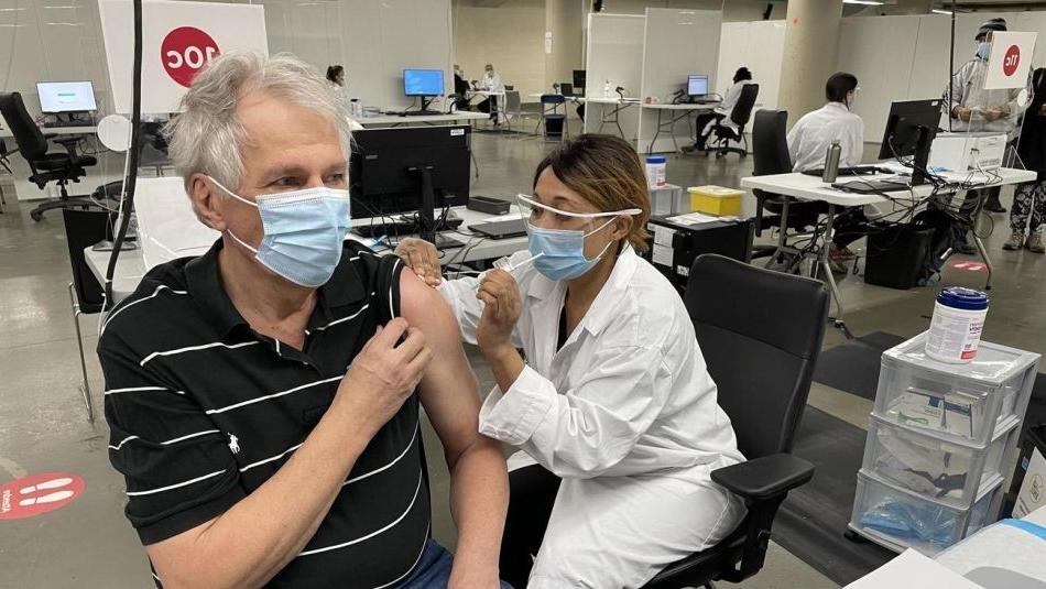 Renaud Gagné戴着口罩，同时在口罩和面罩下接受卫生保健工作者的疫苗接种. 