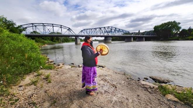 站在河岸上拿着鼓的女人. 背景中可以看到一座桥.