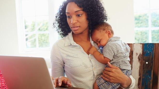 一个女人在电脑前工作时抱着一个婴儿.